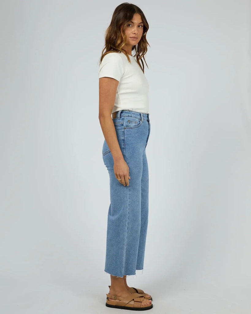 Woman wearing a white t-shirt and blue jeans on a plain background