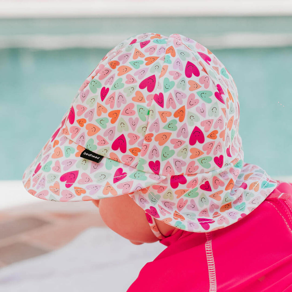 Child wearing a colorful heart-patterned sun hat by a pool.