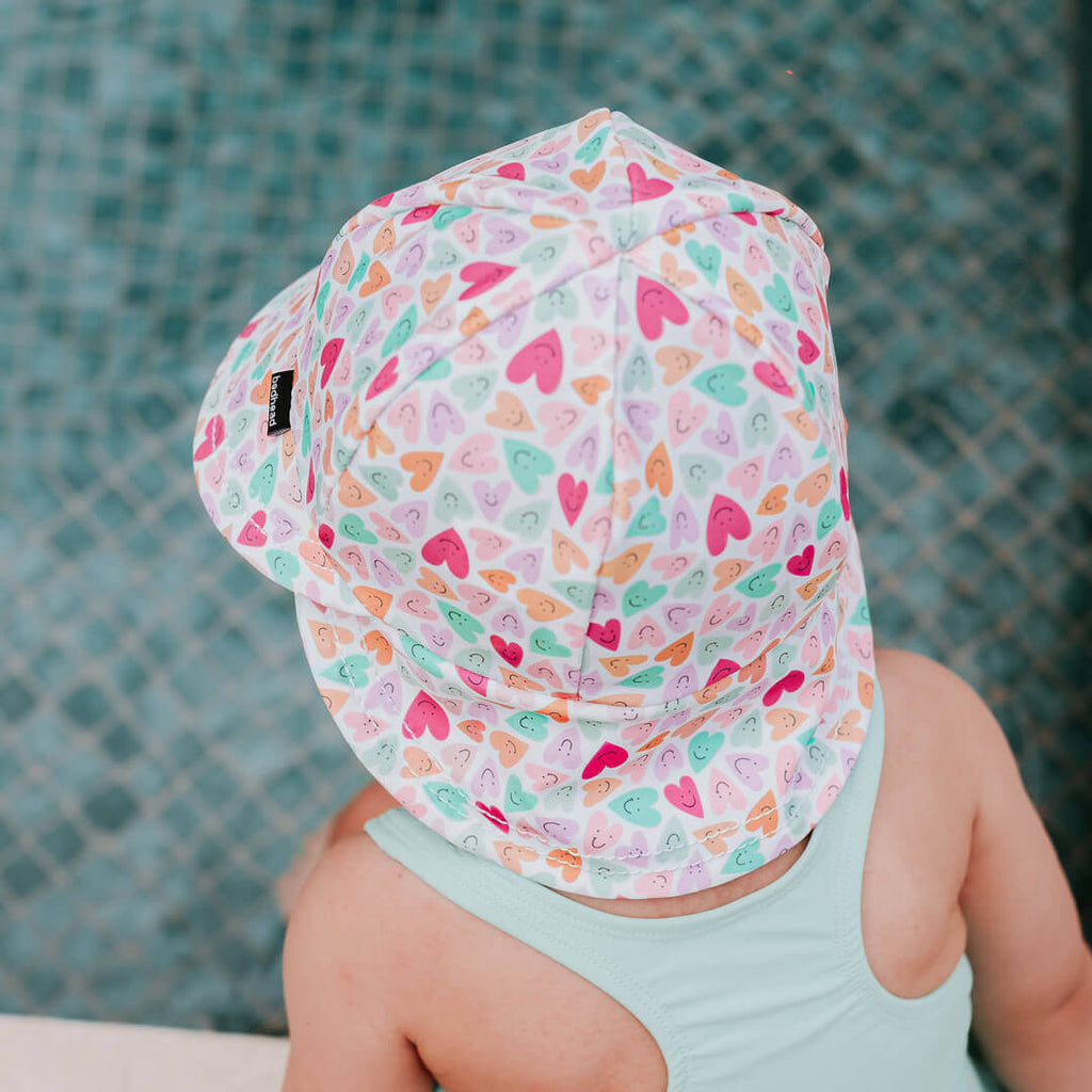 Child wearing a colorful heart-patterned hat by a pool.