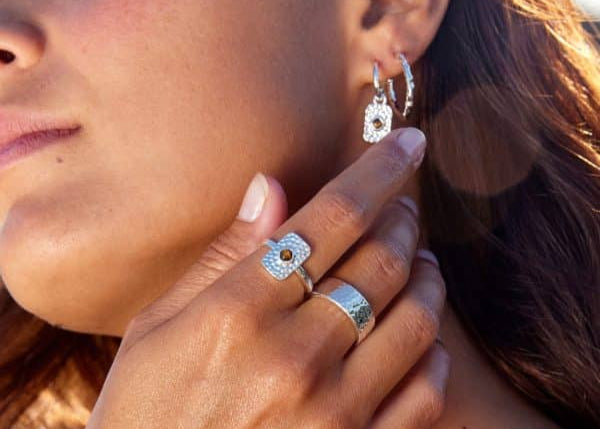 Close-up of a woman wearing silver earrings, ring, and necklace with a blurred background