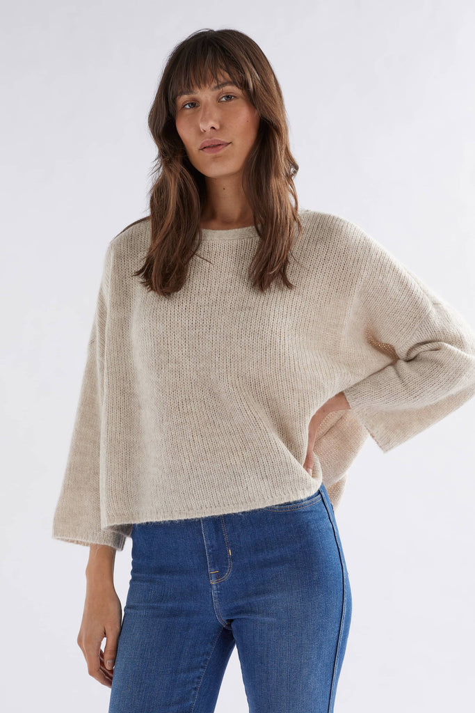 Woman wearing a beige sweater and blue jeans on a white background