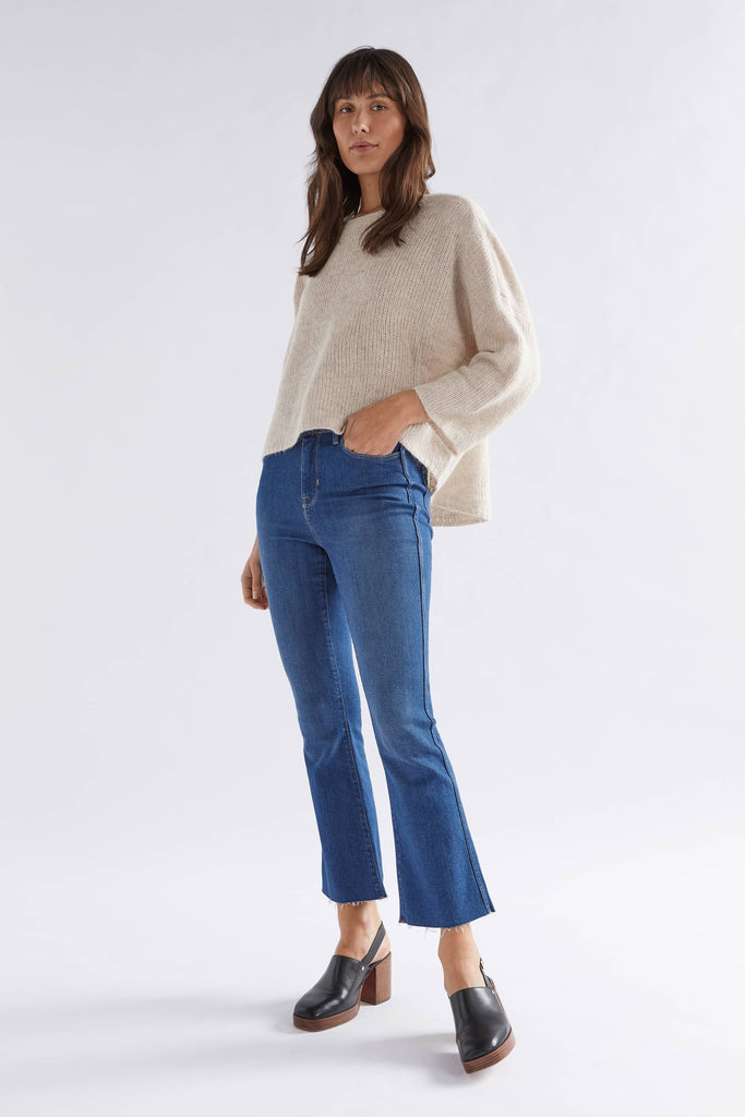 Woman wearing a beige sweater and blue jeans on a white background