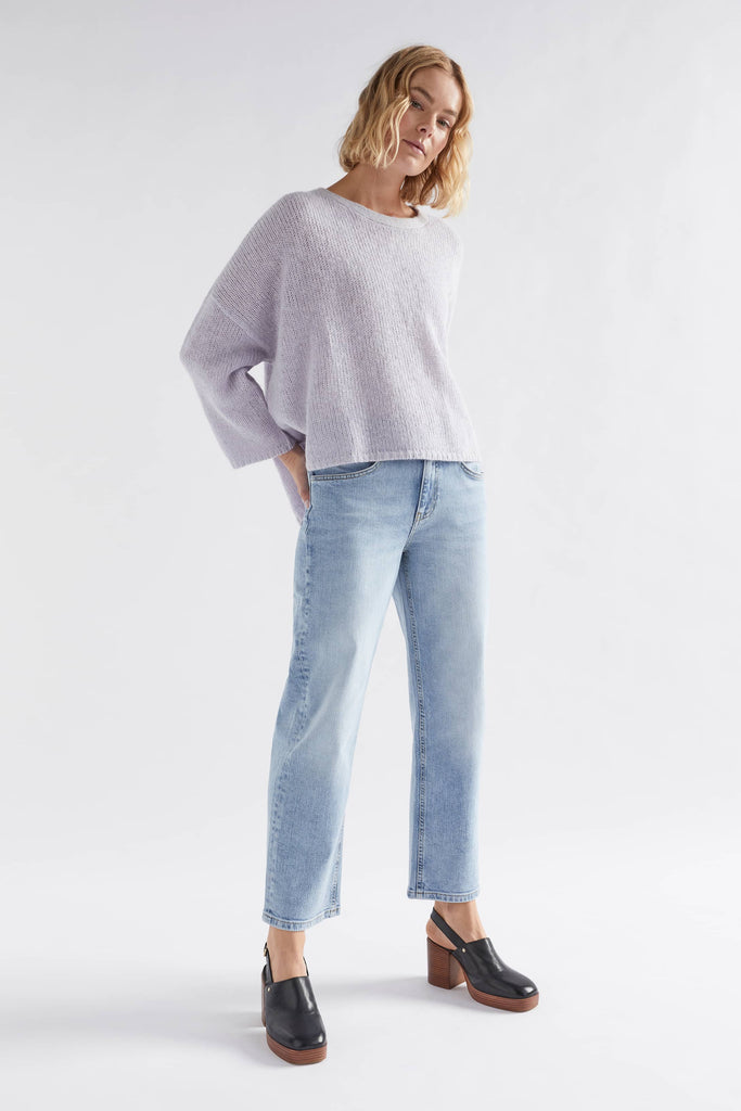 Woman wearing a light gray sweater and blue jeans on a white background