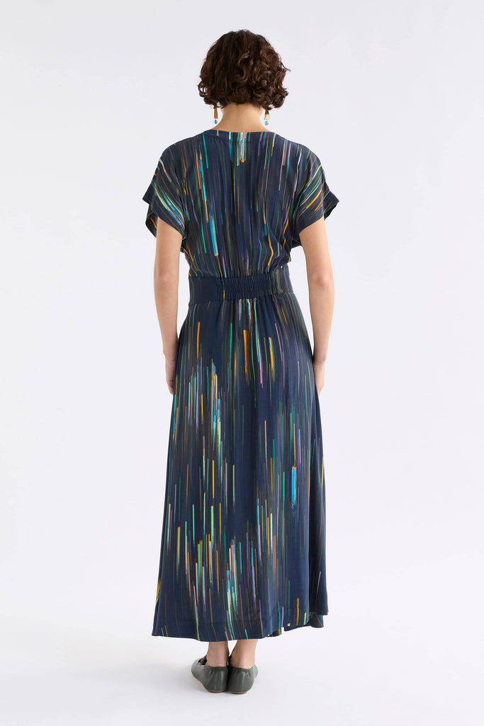 Person wearing a long, dark blue dress with colorful abstract patterns on a white background