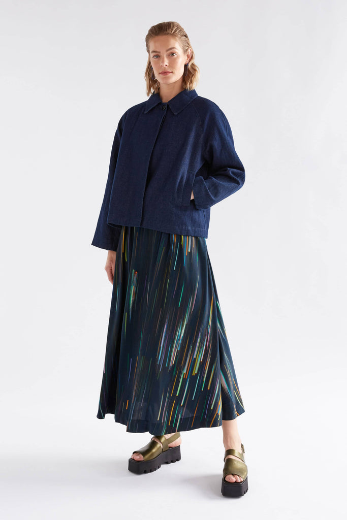 Woman wearing a blue coat and patterned skirt on a white background