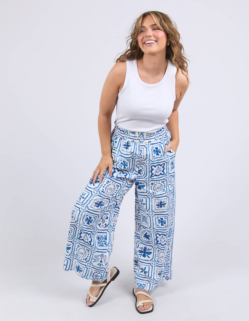 Woman wearing a white tank top and blue patterned pants on a white background