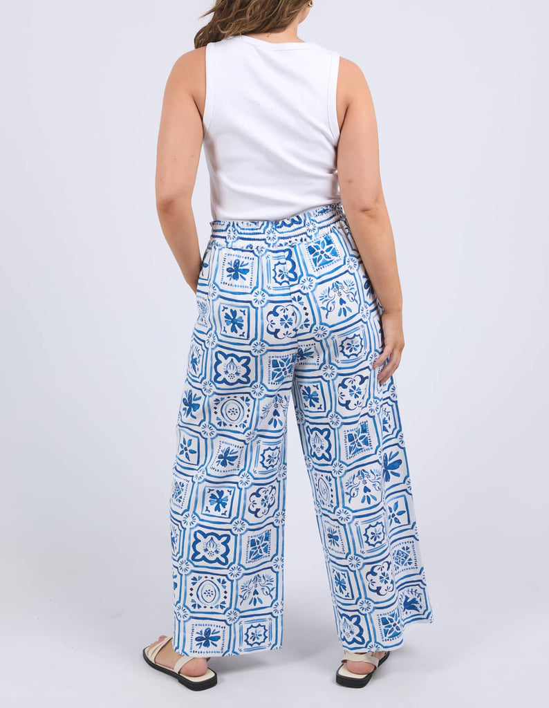 Woman wearing blue patterned pants and a white top on a white background