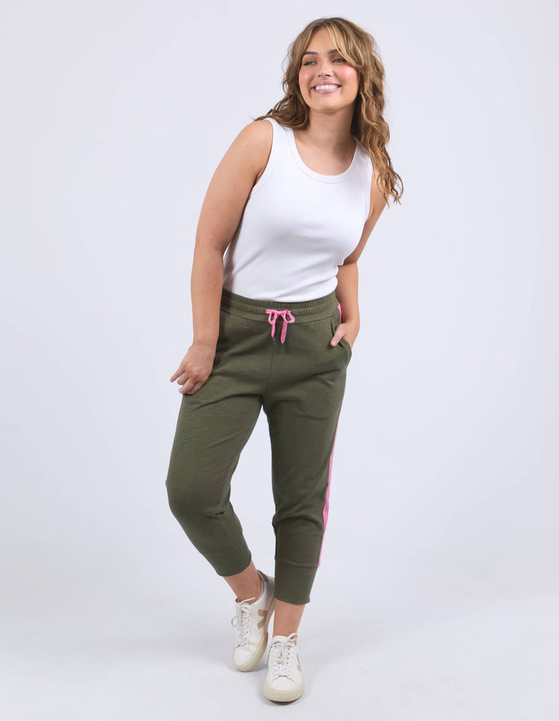 Woman wearing a white tank top and green jogger pants with pink accents on a white background