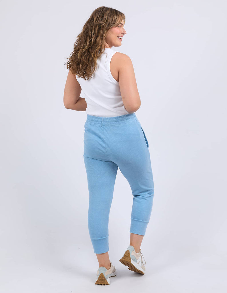 Woman wearing light blue jogger pants and a white top on a white background