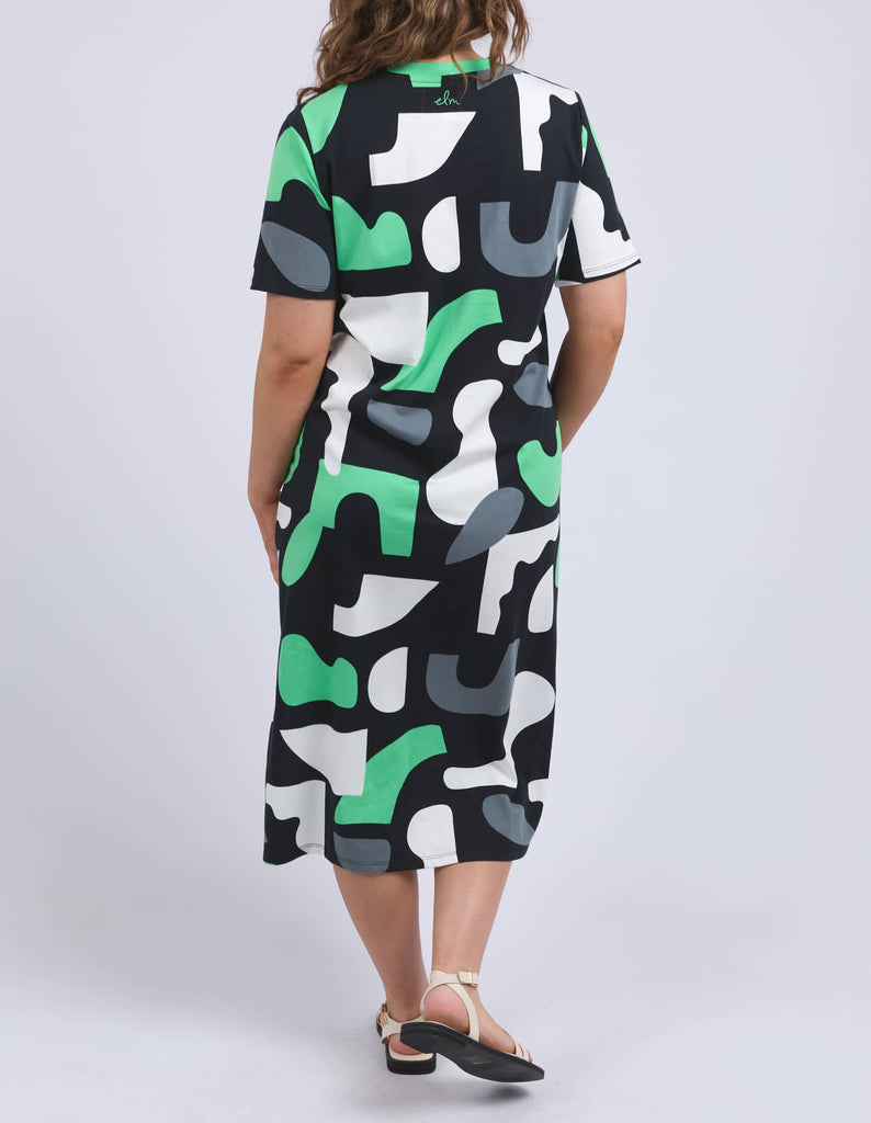 Person wearing a patterned dress with green, black, and white design on a plain background
