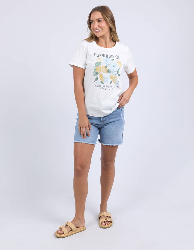 Woman wearing a white t-shirt with floral design and denim shorts on a plain background
