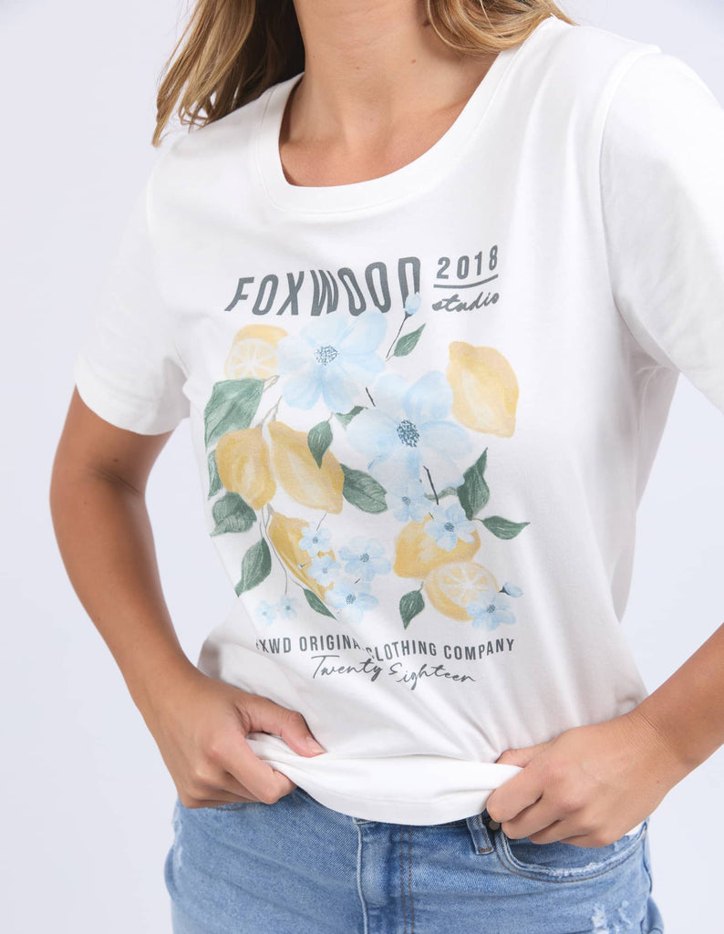 White t-shirt with floral and lemon design, worn by a person on a light gray background