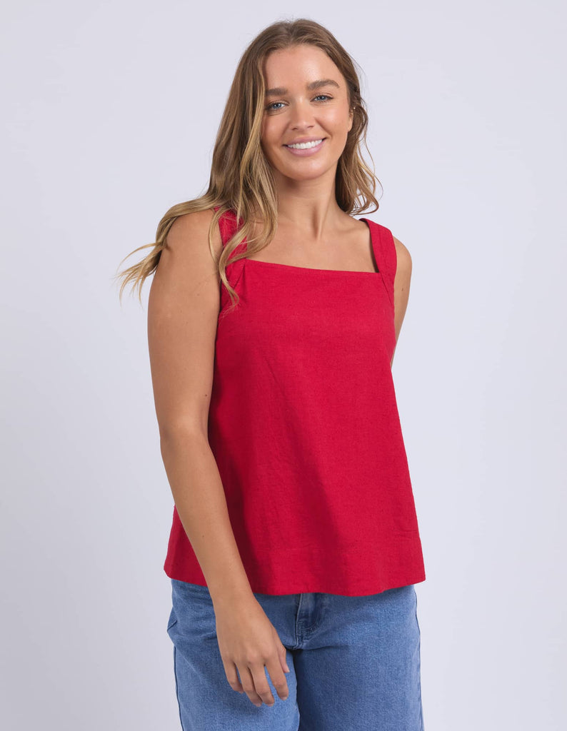 Woman wearing a red tank top and blue jeans on a white background