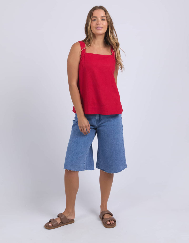 Woman wearing a red tank top and blue shorts on a white background