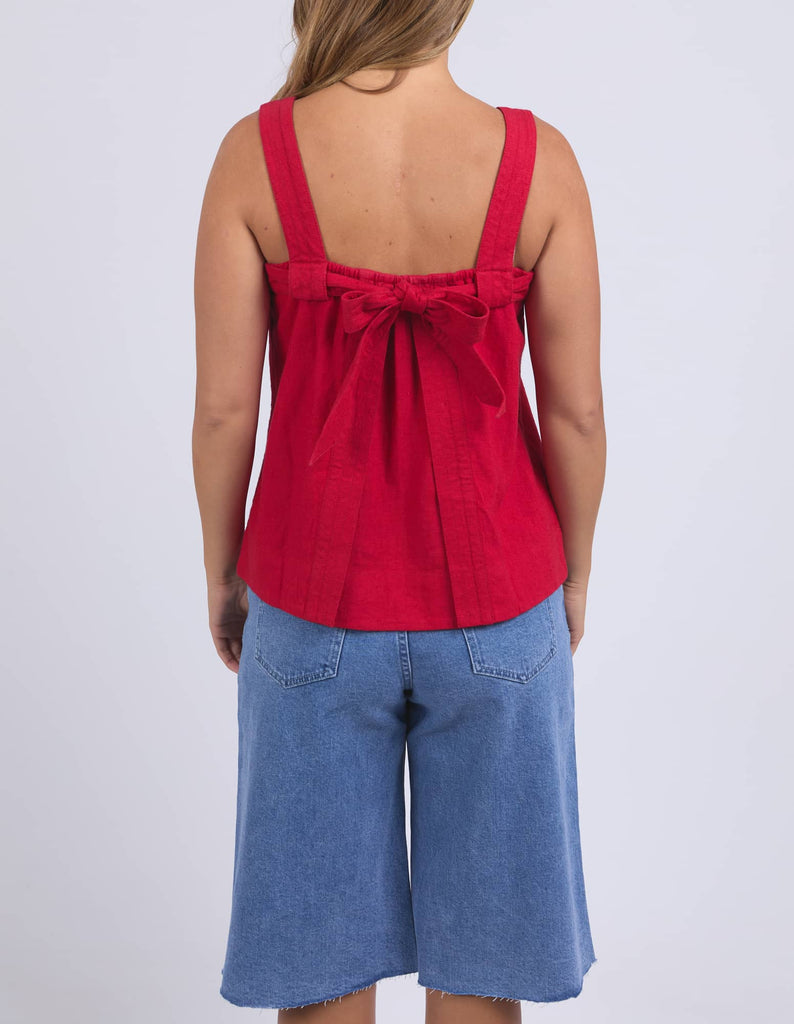 Person wearing a red tank top with a bow detail and blue denim shorts on a white background