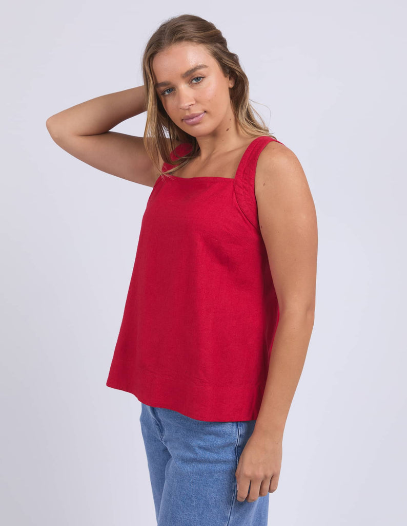 Woman wearing a red sleeveless top and blue jeans on a white background