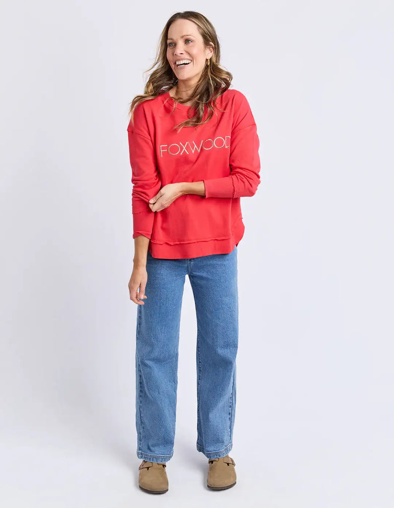 Woman wearing a red 'FOXWOOD' hoodie and blue jeans on a white background