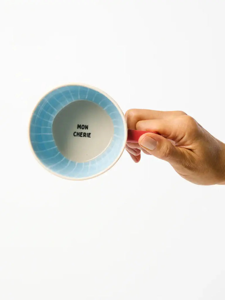Hand holding a ceramic mug with 'MON CHERIE' text on a white background