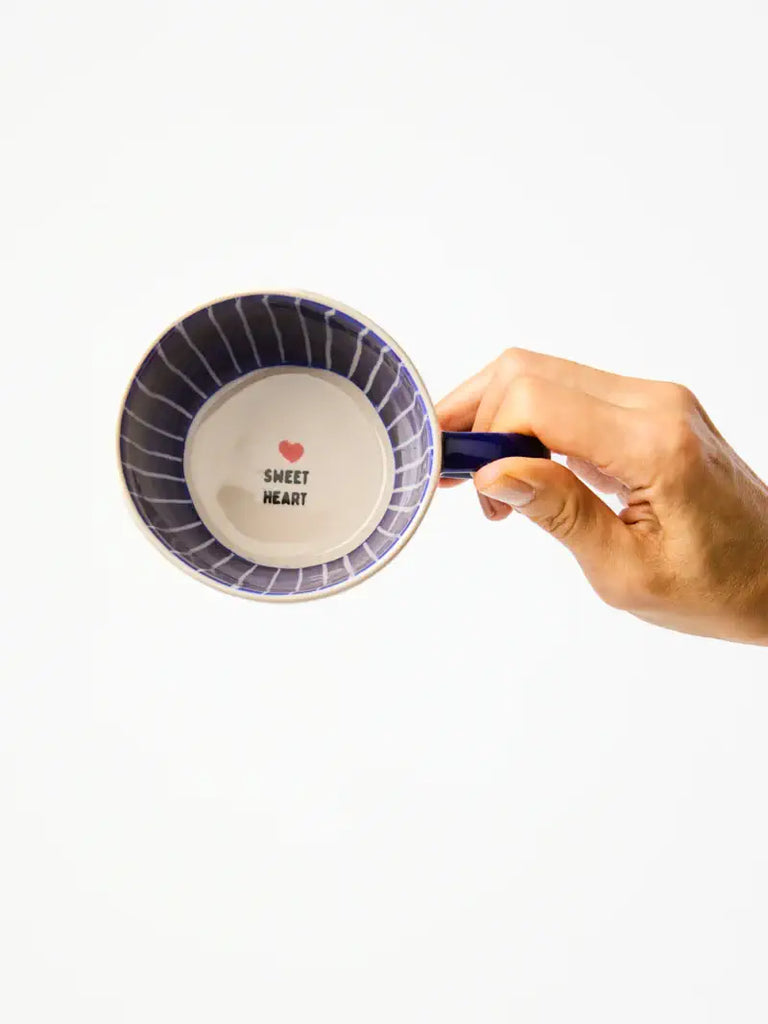 Hand holding a small decorative plate with 'sweet heart' text and a red heart symbol on a white background.