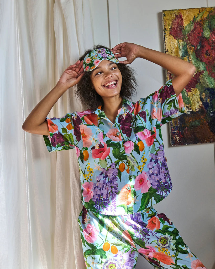 Woman wearing a colorful floral pajama set and headband, smiling in a room with a painting in the background.