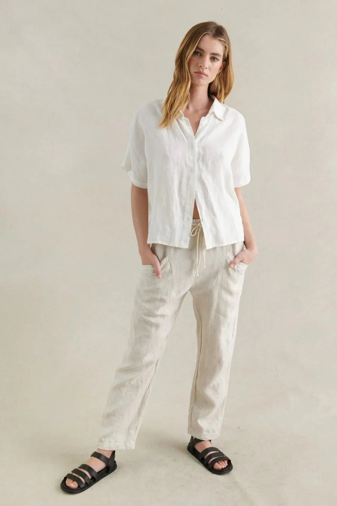 Woman wearing a white shirt and beige pants against a plain background