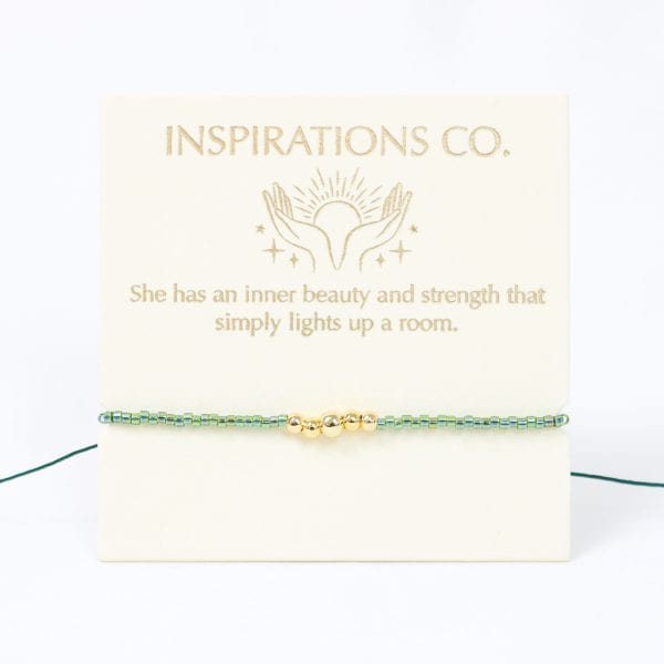 Bracelet with gold and green beads on a card with 'Inspirations Co.' text