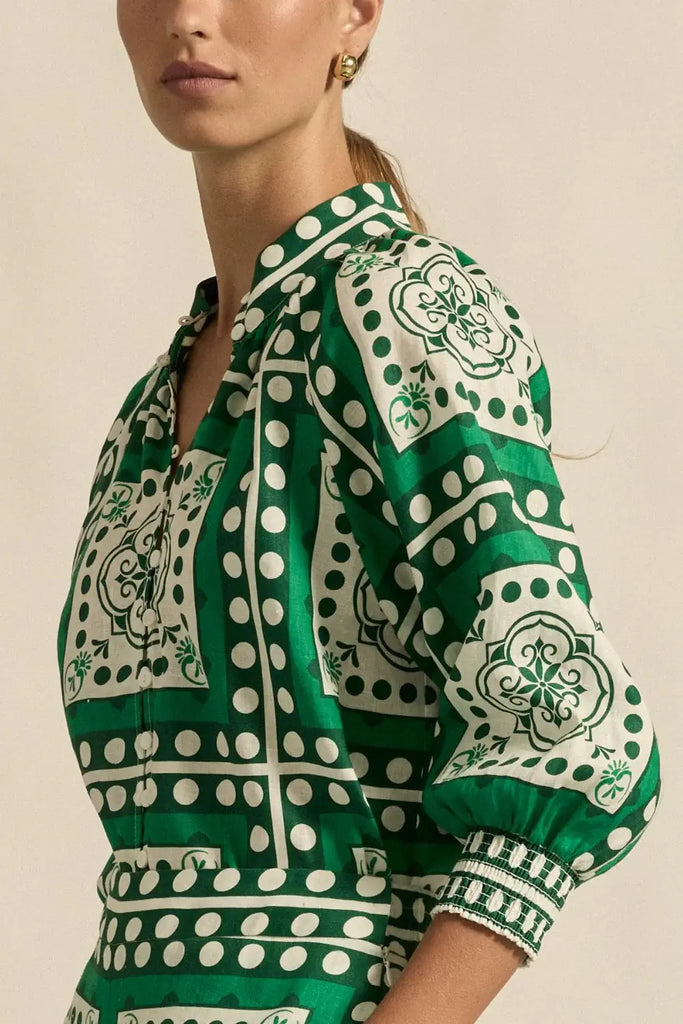 Green and white patterned blouse worn by a person on a beige background
