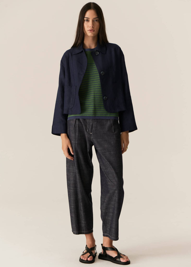 Woman wearing a navy jacket, green striped shirt, and dark pants on a beige background