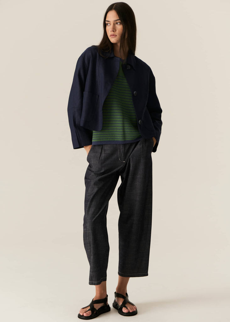 Woman wearing a navy jacket, green striped shirt, and dark pants on a beige background