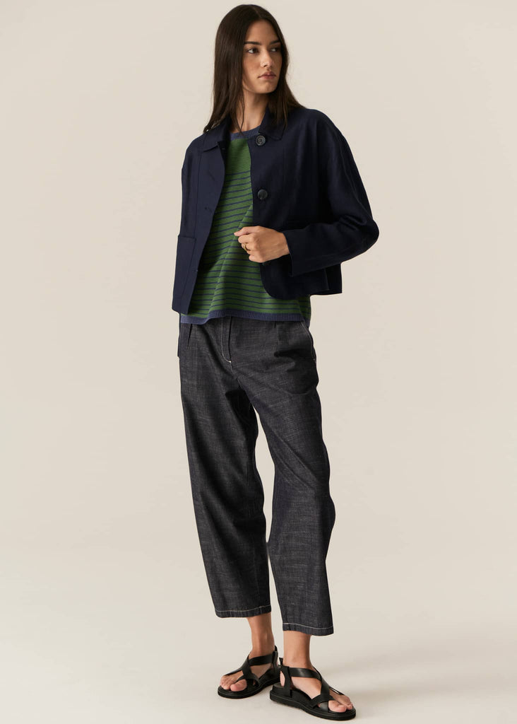 Woman wearing a navy jacket, green striped shirt, and dark pants on a beige background