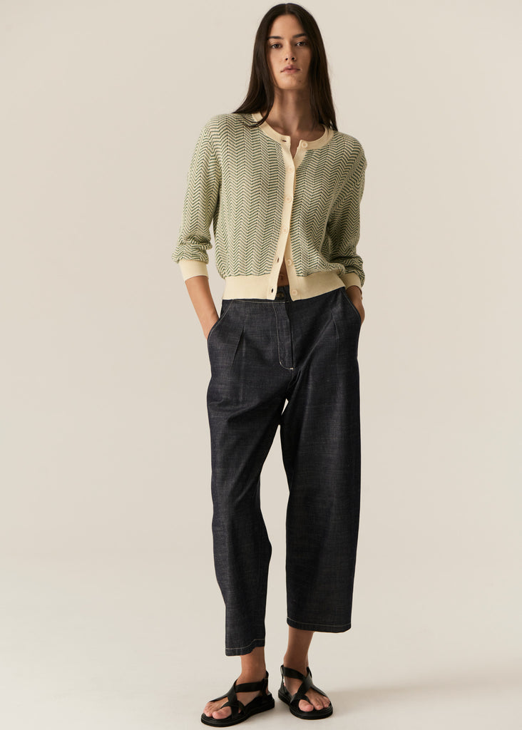 Woman wearing a green patterned cardigan and dark pants on a beige background
