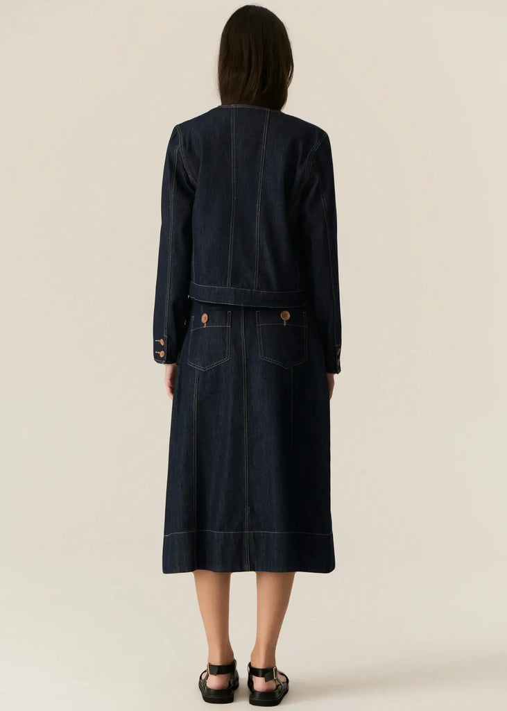 Person wearing a dark denim jacket and skirt set on a beige background
