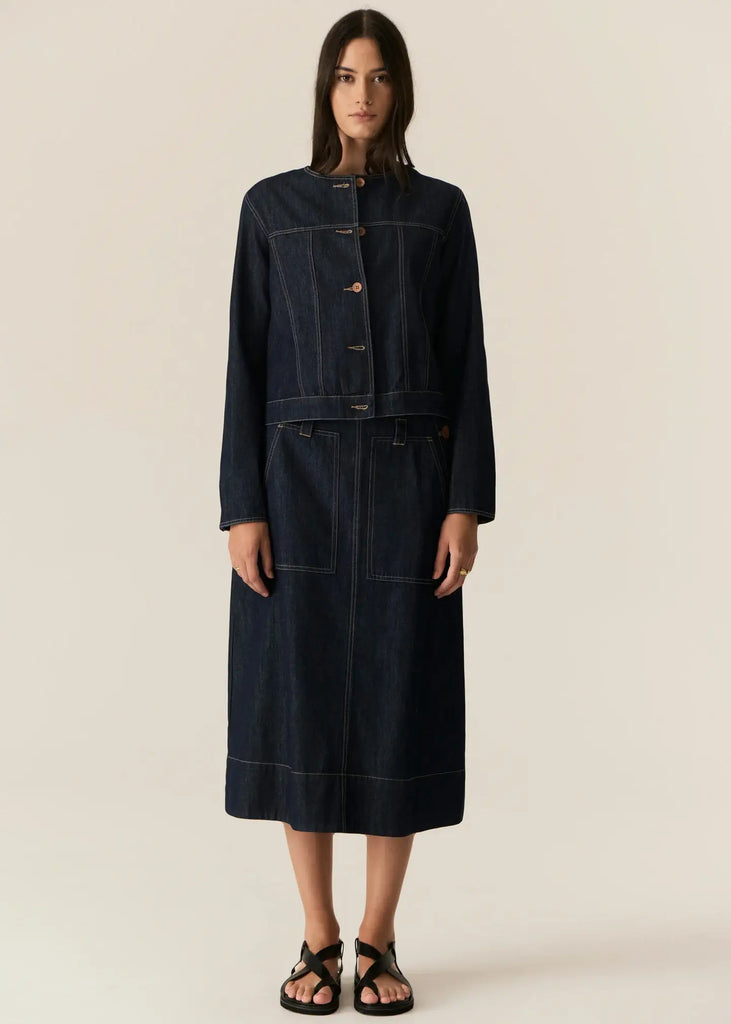 Woman wearing a dark denim jacket and skirt set on a beige background