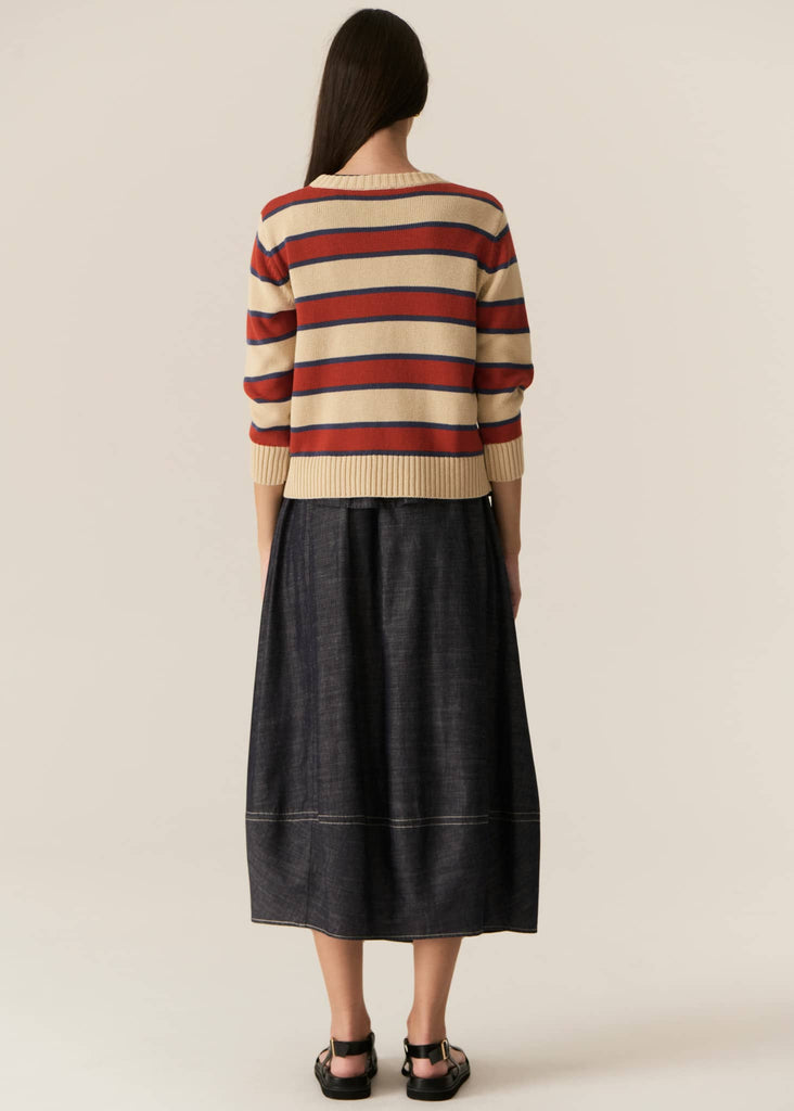 Person wearing a striped sweater and black skirt on a beige background