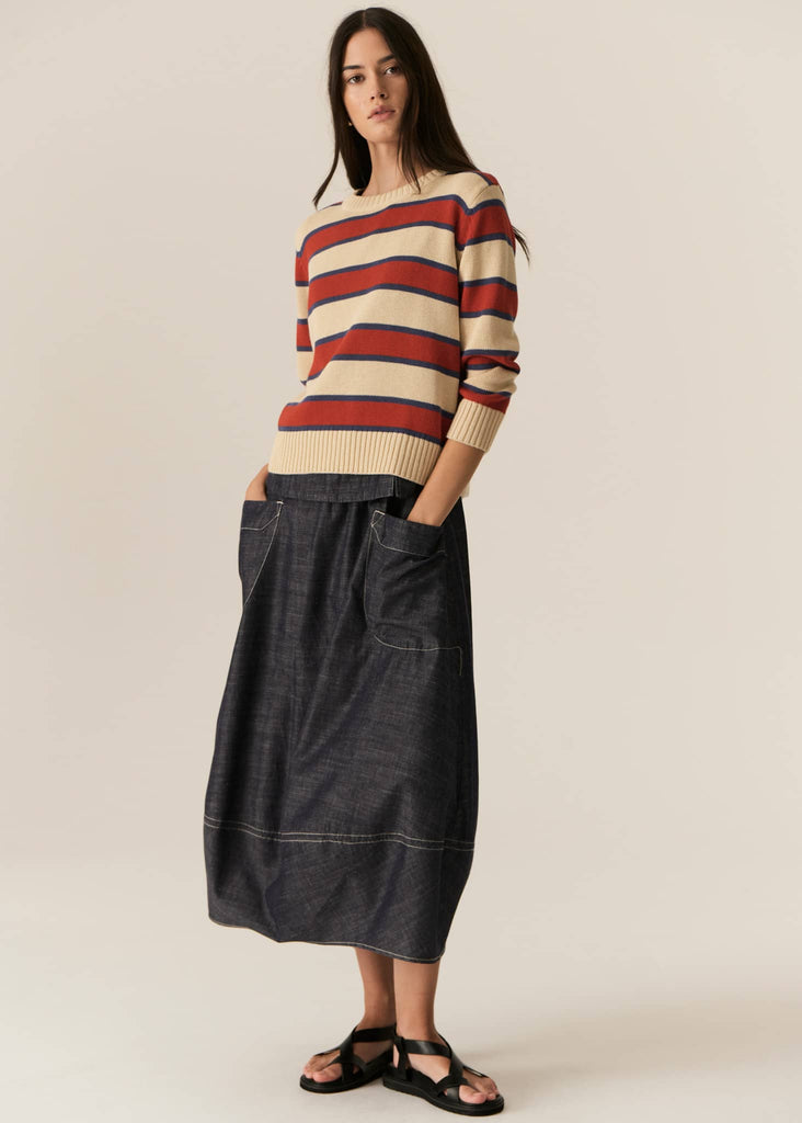 Woman wearing a striped sweater and denim skirt on a plain background