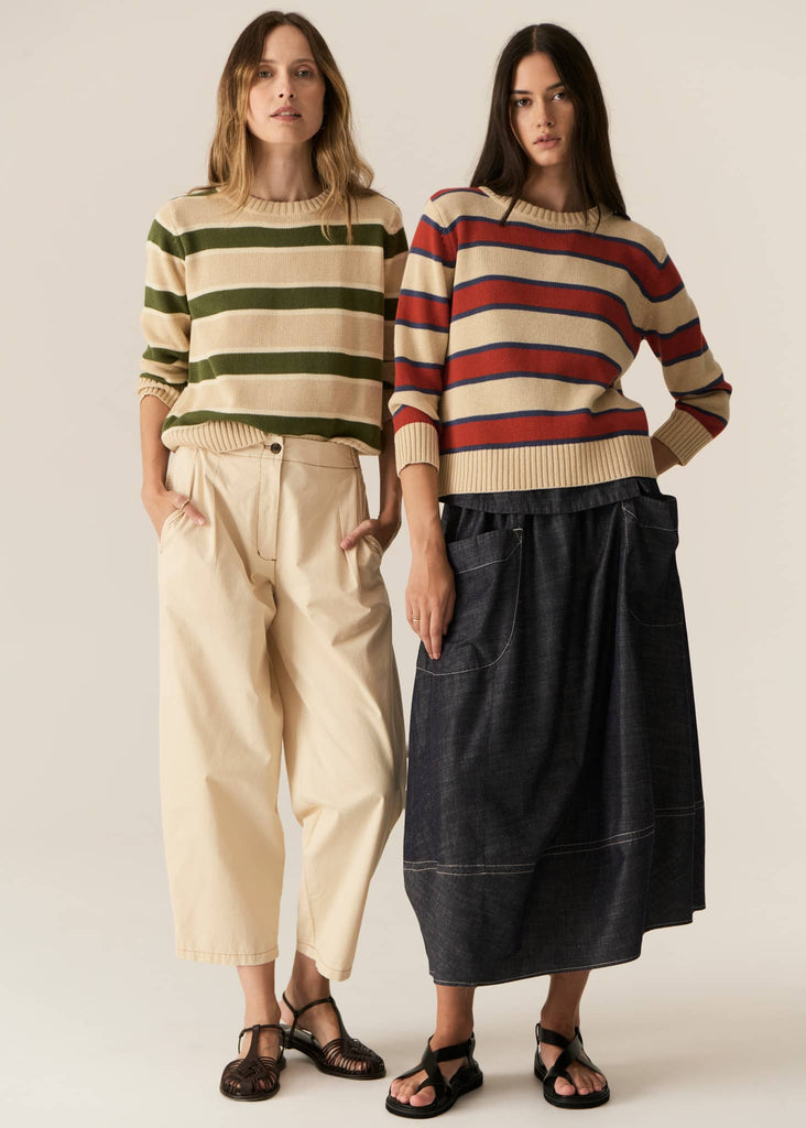 Two women wearing striped sweaters and pants on a plain background