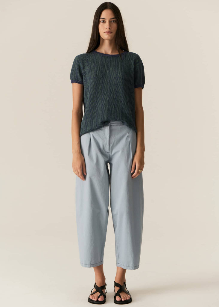 Woman wearing a dark green t-shirt and light blue pants on a beige background