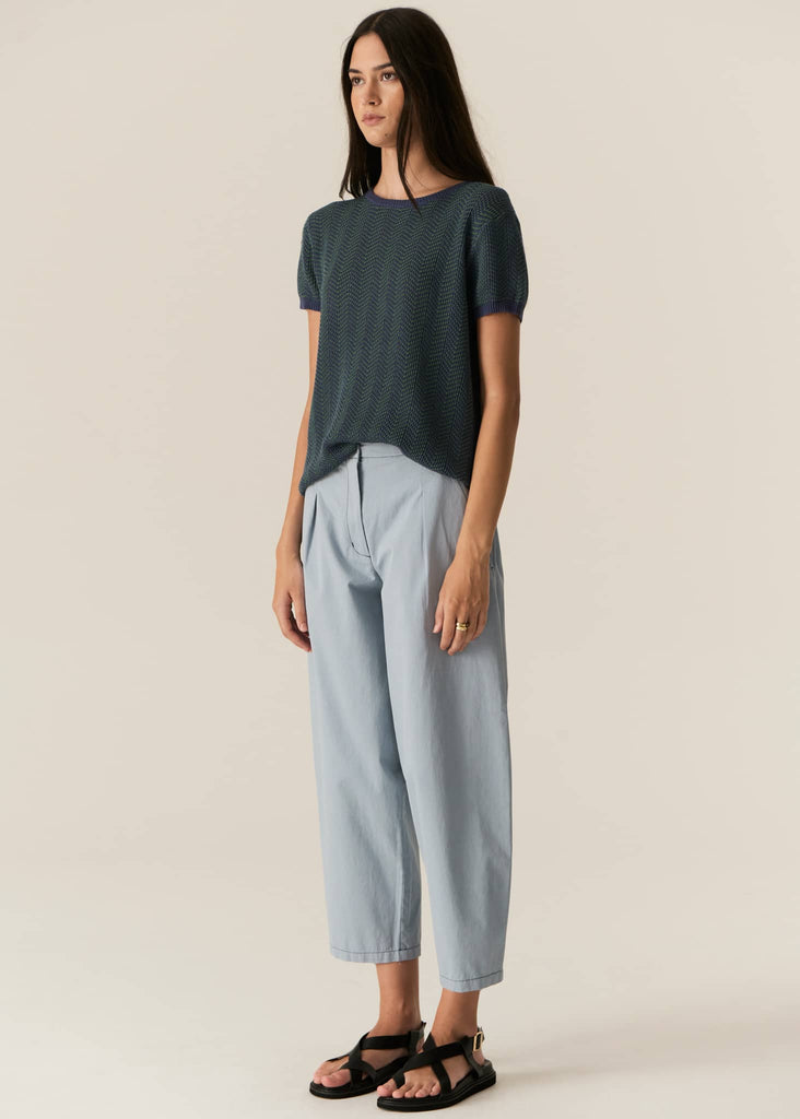 Woman wearing a dark green t-shirt and light blue pants on a beige background