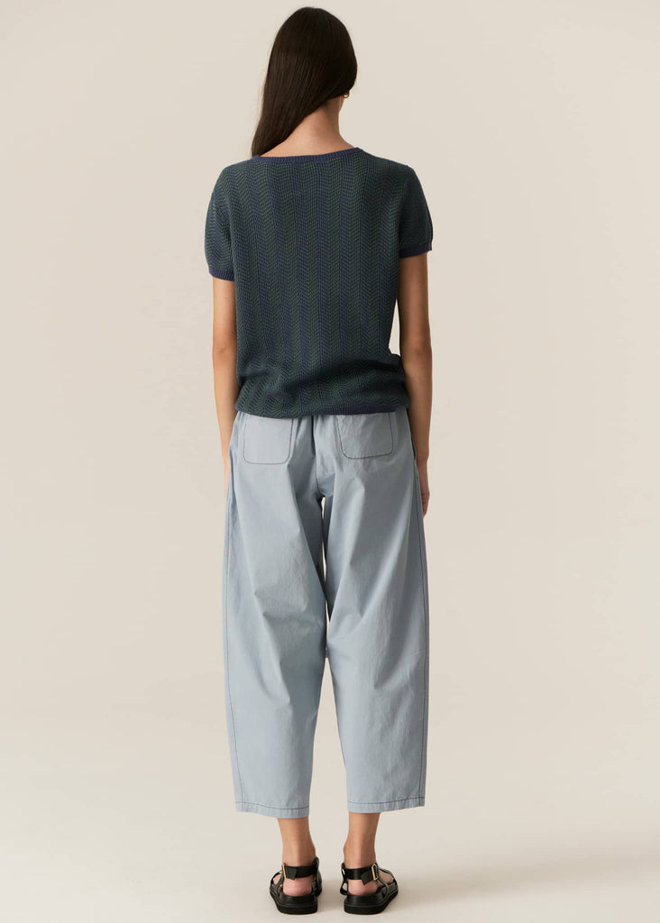 Person wearing a dark green top and light blue pants on a beige background