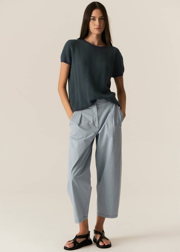 Woman wearing a dark blue t-shirt and light gray pants on a beige background