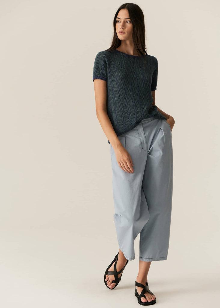 Woman wearing a dark green top and light gray pants on a beige background