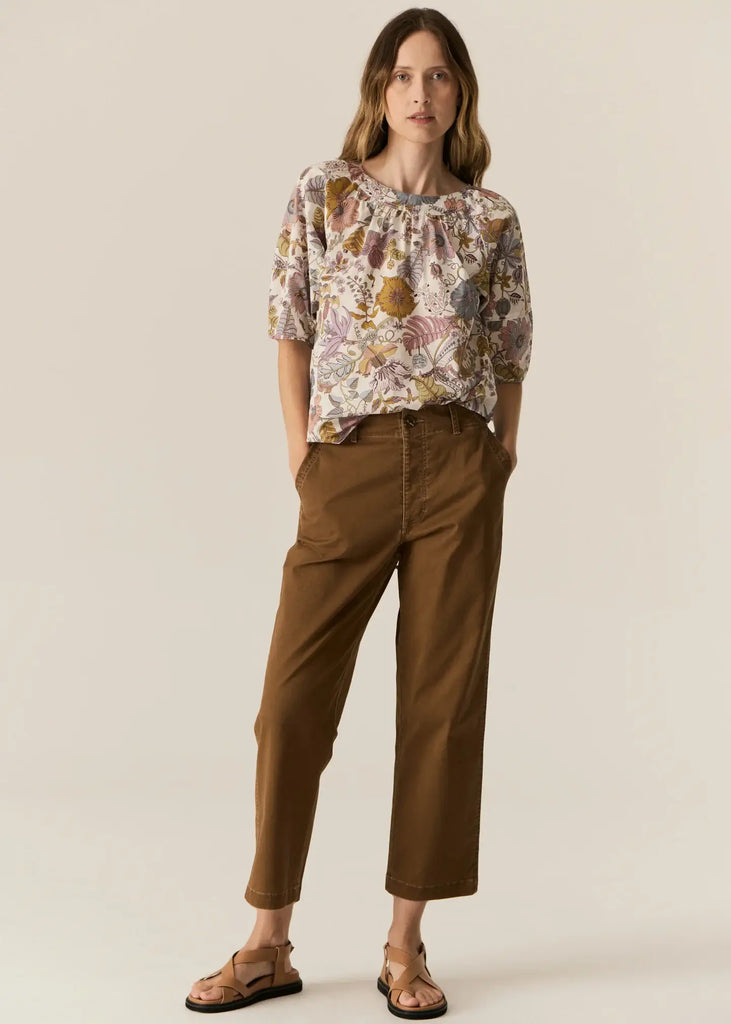 Woman wearing a floral blouse and brown pants on a beige background