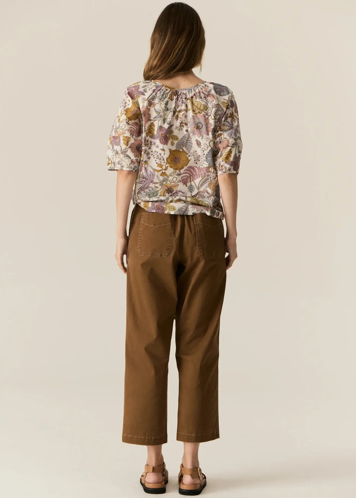 Woman wearing a floral blouse and brown pants on a beige background