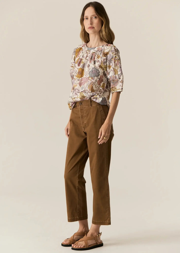 Woman wearing a floral blouse and brown pants on a beige background