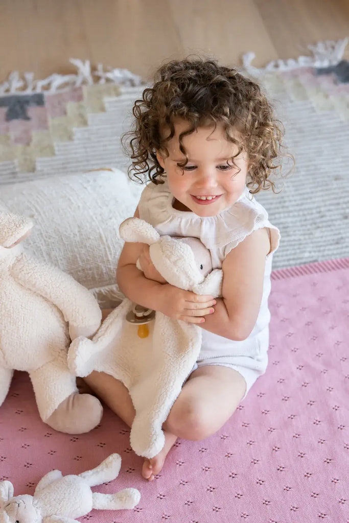 Child holding a teddy bear in a room with pink floor and white furniture