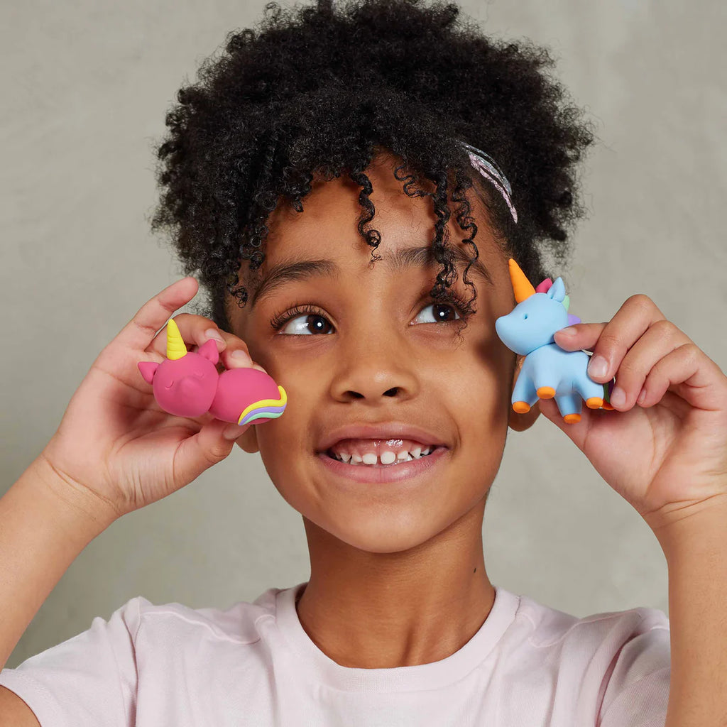 Child holding two colorful rubber duckies near their ears against a neutral background
