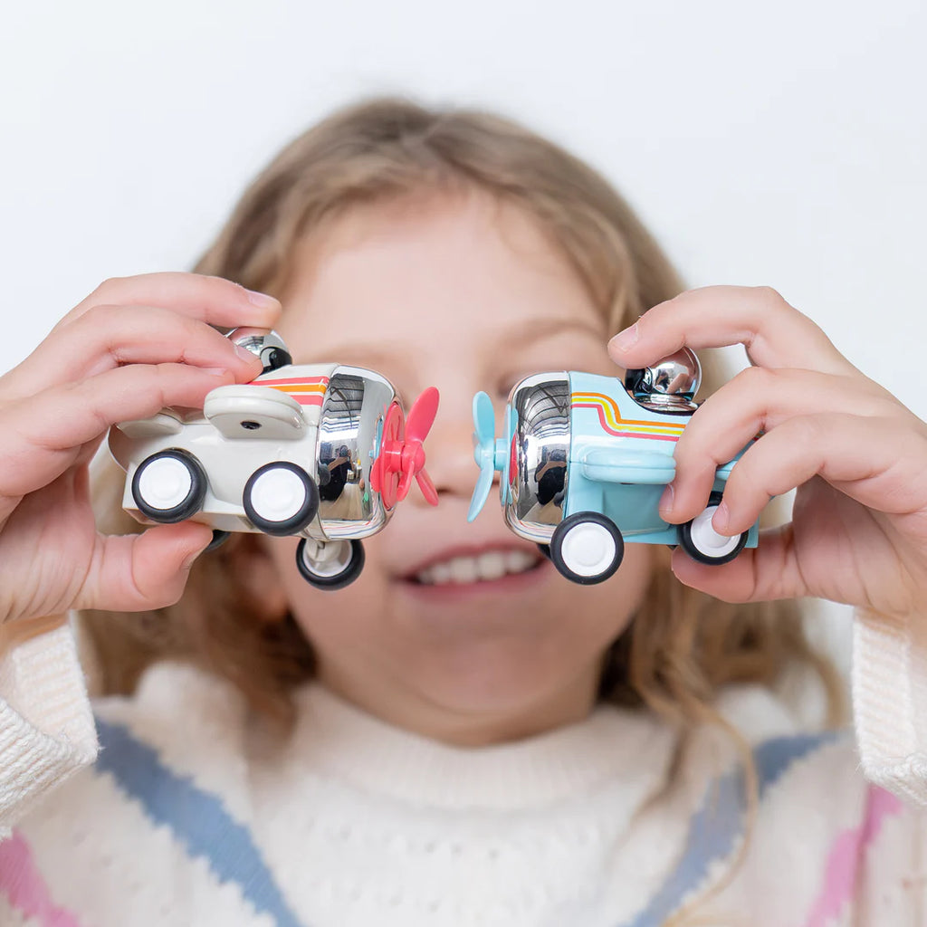Child holding two toy cars up to their eyes against a white background
