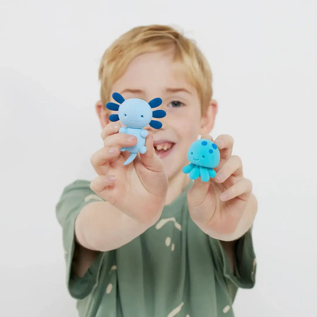 Child holding two blue cartoon-like figurines against a white background