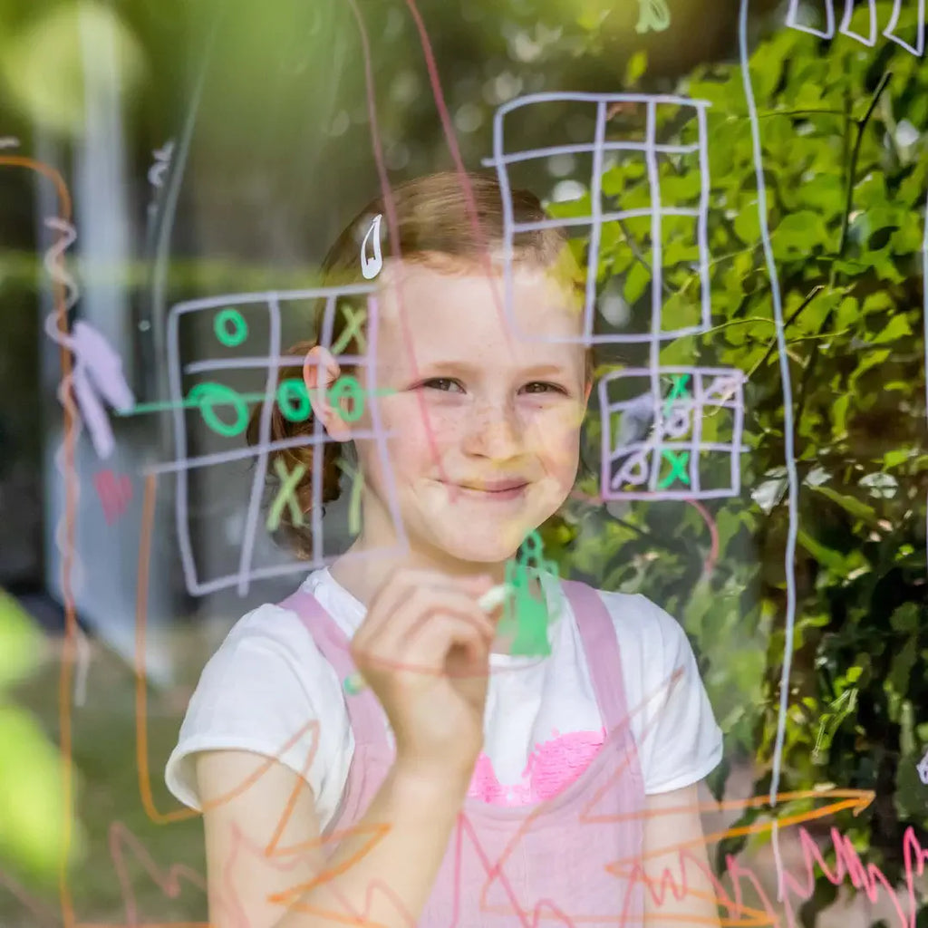 Young girl in front of a window with colorful drawings