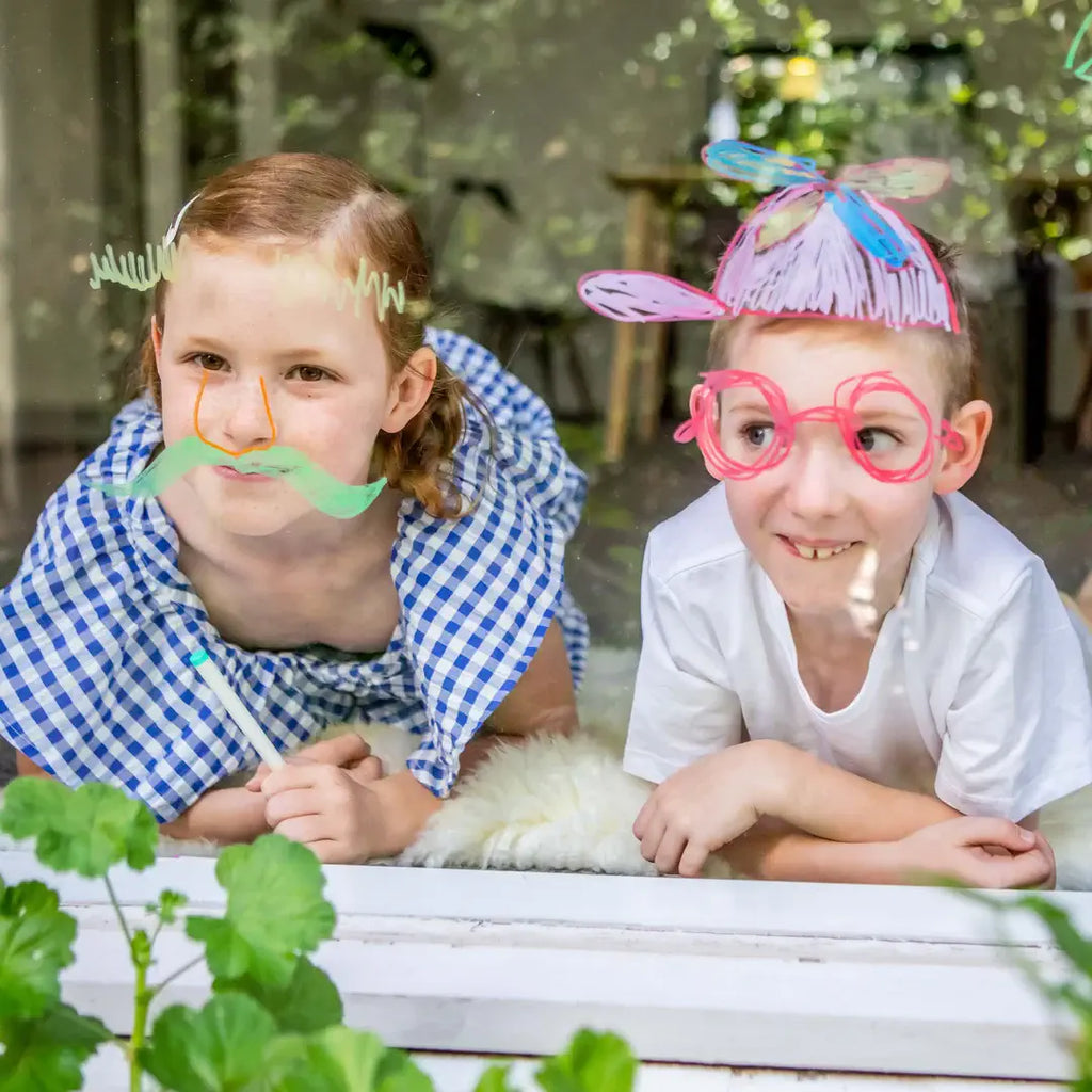 Two children wearing novelty glasses and hats outdoors.